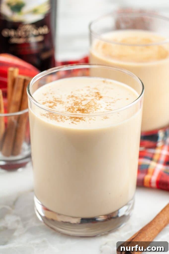 Short glass of eggnog cocktail, garnished with a sprinkle of cinnamon and nutmeg, on a festive holiday background.