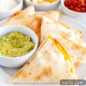 Crispy quesadilla triangles arranged on a plate next to a bowl of fresh guacamole.