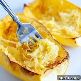 Perfectly cooked spaghetti squash strands being pulled with a fork, ready to be seasoned.
