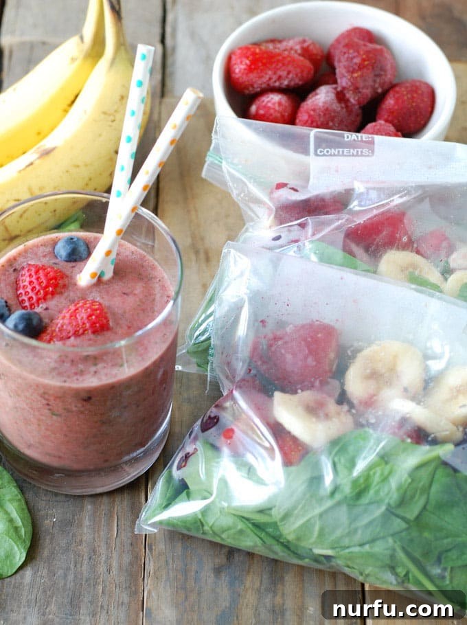 Freezer Smoothie An assortment of fresh and frozen ingredients for a smoothie, including a bag of spinach, sliced banana, strawberries, and blueberries, neatly organized for meal prep.