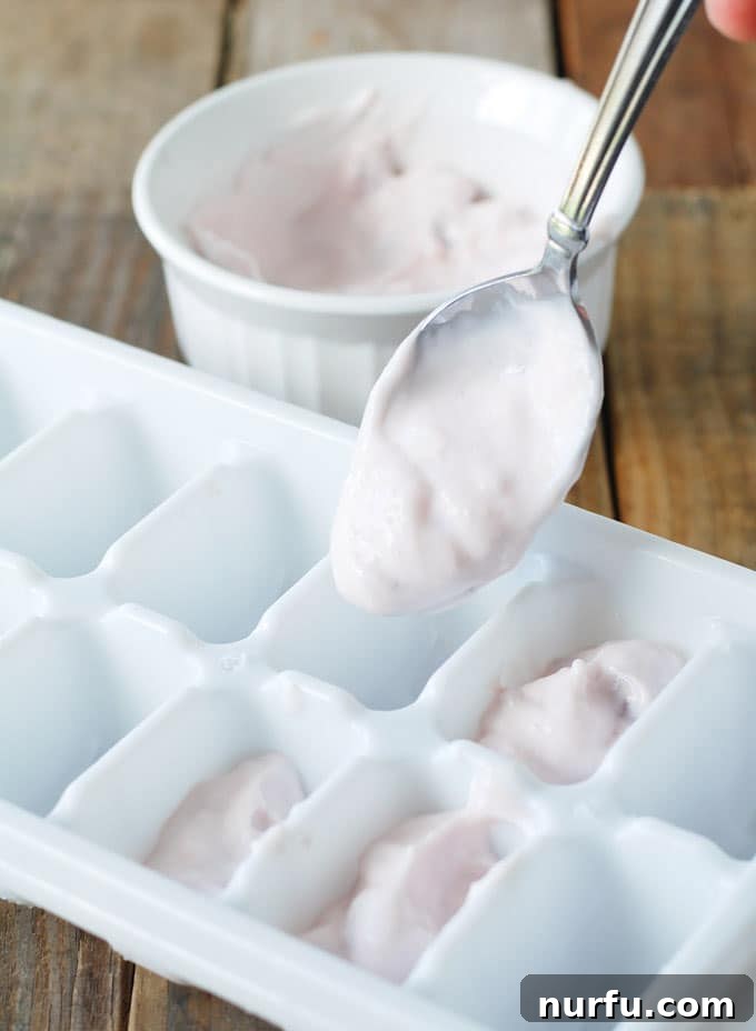Freezer Smoothie Pack Strawberry Greek yogurt being carefully spooned into ice cube trays, a crucial step for preparing convenient frozen yogurt cubes.