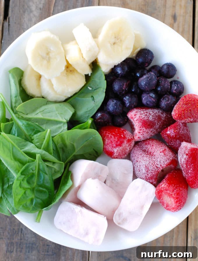 Freezer Smoothie Pack A bowl filled with various smoothie ingredients, including fresh spinach, sliced banana, blueberries, strawberries, and frozen yogurt cubes, organized and ready for assembly into freezer packs.