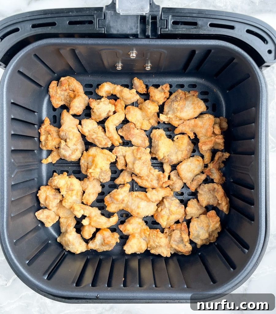 Crispy Trader Joes Orange Chicken Air Fryer 4 Crispy chicken pieces sizzling inside the air fryer basket during the cooking process.