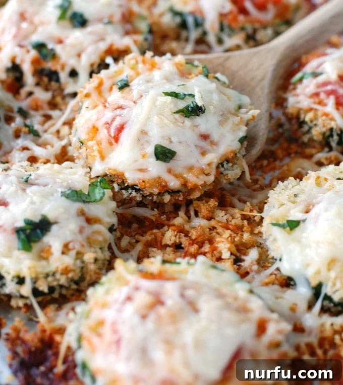 Cheesy Baked Zucchini Parmesan 2 Slices of zucchini covered in melted cheese, fresh basil garnish on a baking sheet, ready to be served.