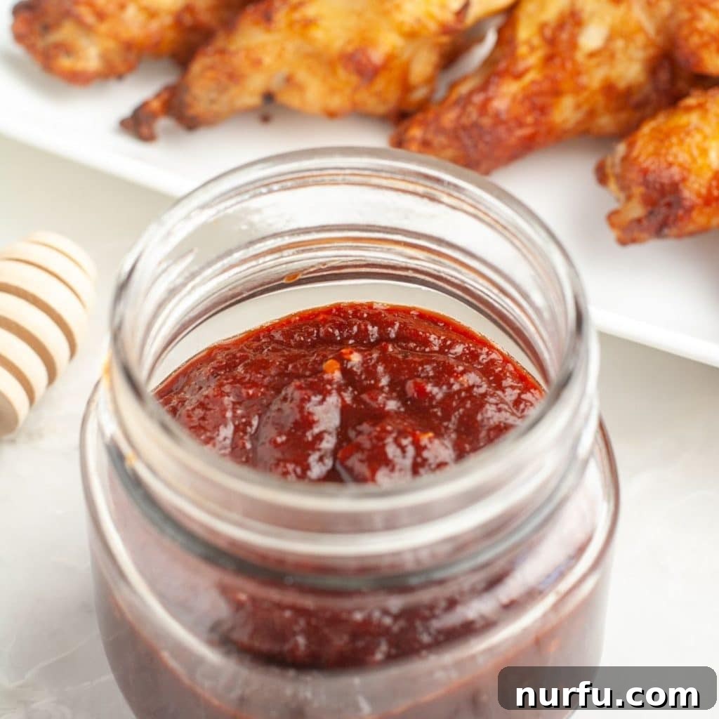 Sweet and Smoky Honey Chipotle Sauce 2 Jar of rich, red honey chipotle sauce, with blurred chicken wings in the background, suggesting a delightful meal.