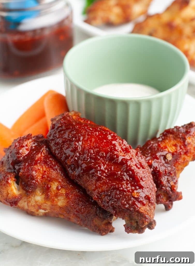 Sweet and Smoky Honey Chipotle Sauce 6 Plate of crispy chicken wings coated in honey chipotle sauce, with a small bowl of ranch dipping sauce in the background.