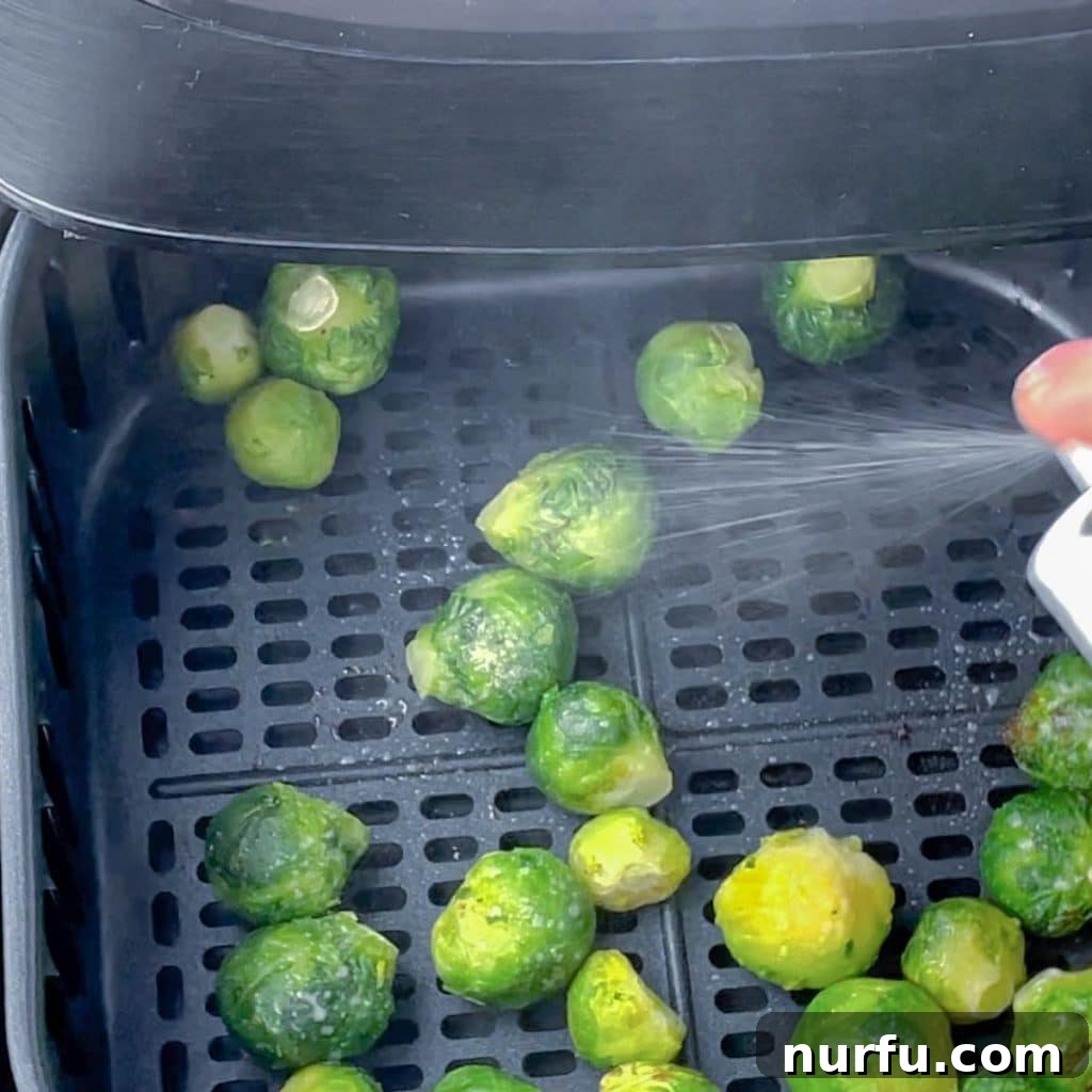 Crispy Air Fryer Frozen Brussels Sprouts Made Easy 5 Olive oil being misted onto brussels sprouts in an air fryer basket.
