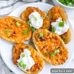 Plate of golden-brown potato skins with melted cheese, sour cream, and a garnish of fresh chives.