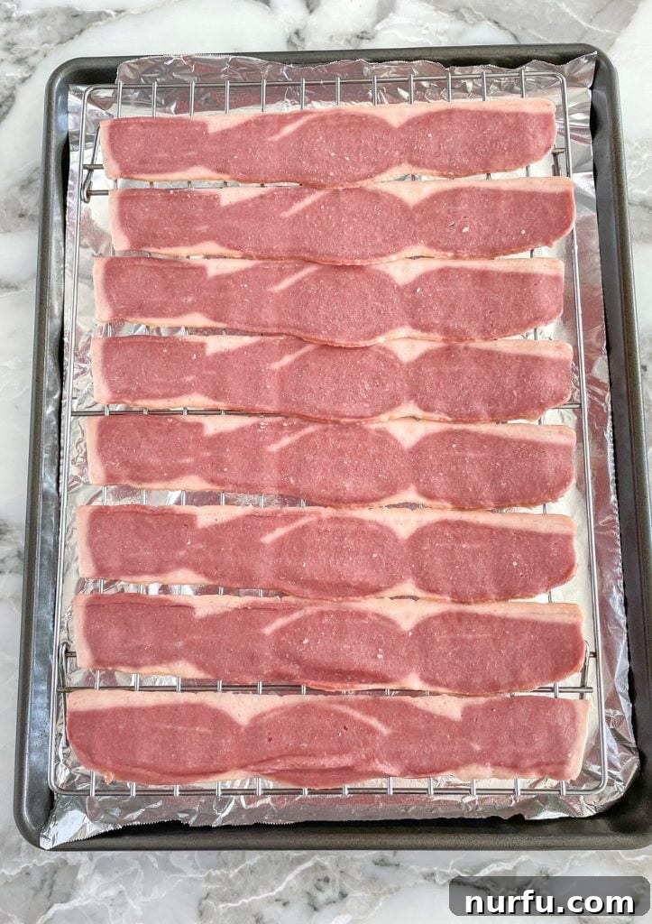 Crispy Oven Turkey Bacon 3 Raw turkey bacon slices neatly arranged in a single layer on a wire rack over a foil-lined baking sheet, ready for the oven.