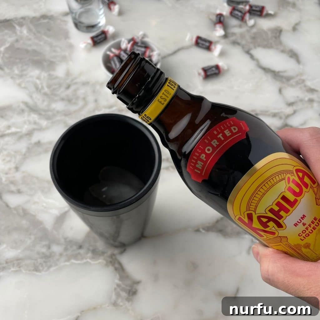 A bottle of Kahlua pouring coffee liqueur into a cocktail shaker filled with ice.