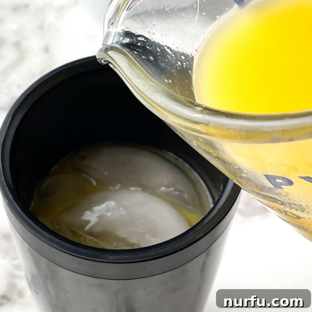 Orange juice being poured into a cocktail shaker with other ingredients, preparing for a Tootsie Roll drink.