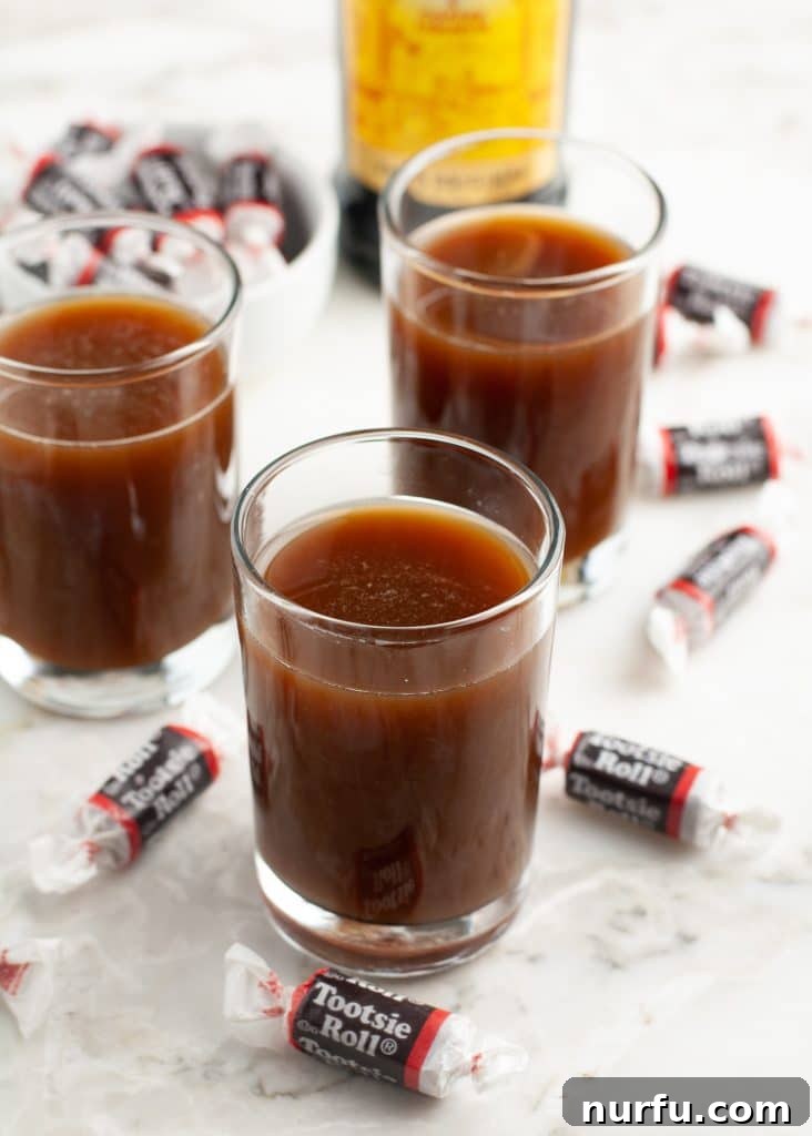 Three shot glasses full of dark Tootsie Roll drinks, each with a Tootsie Roll candy for garnish.