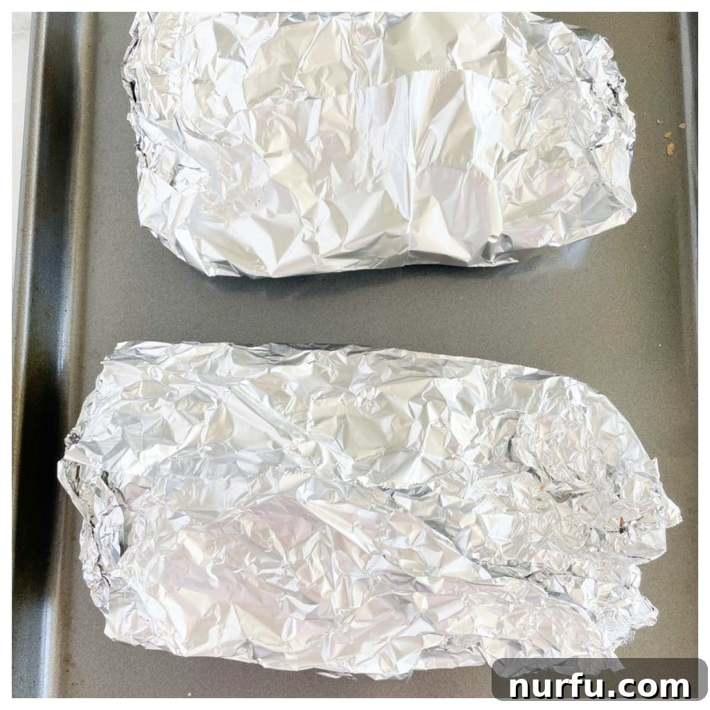 Fall-Off-The-Bone Oven Ribs 6 Foil-wrapped ribs resting on a baking sheet, ready for the oven to begin the slow cooking process.