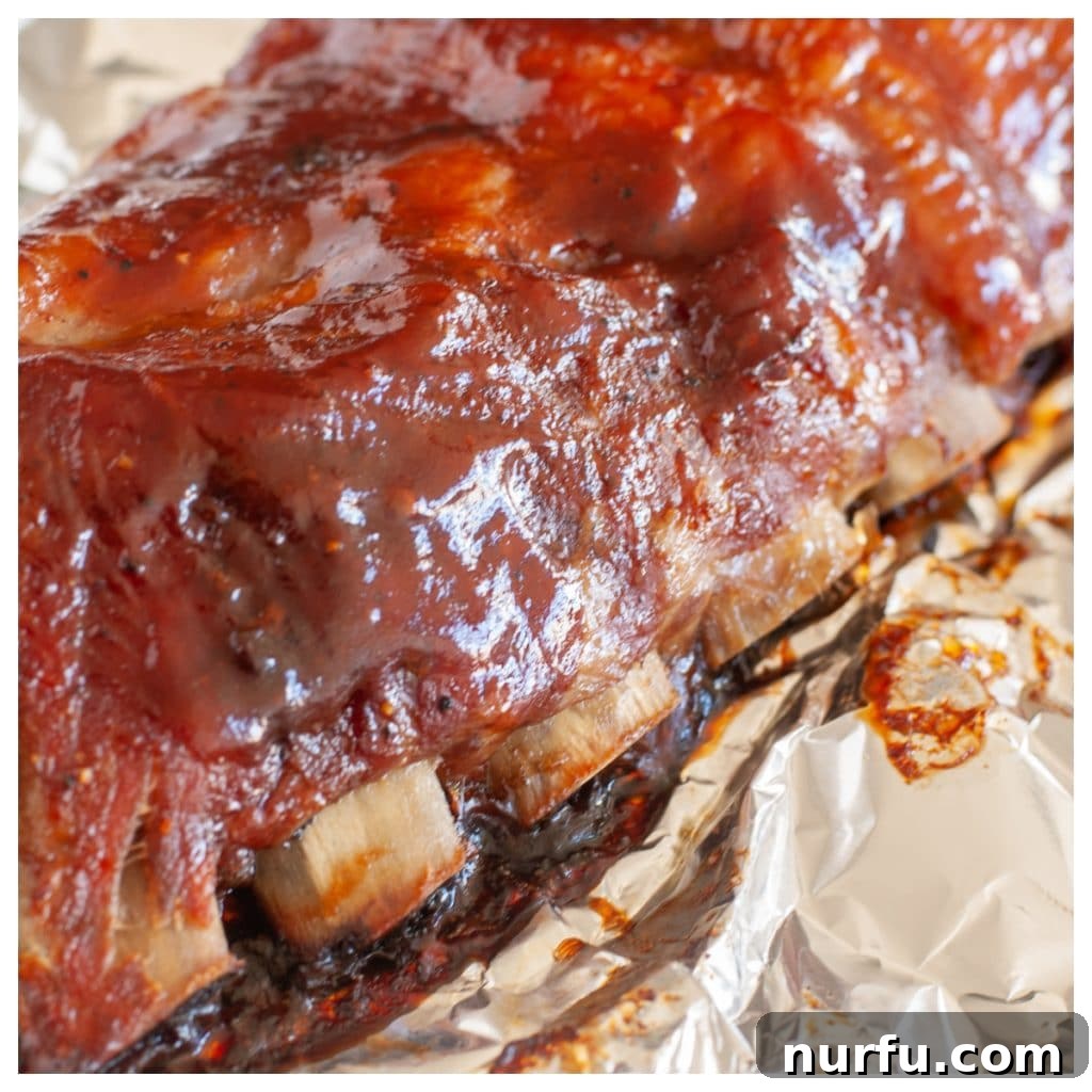 Fall-Off-The-Bone Oven Ribs 7 Succulent cooked ribs with a generous coating of BBQ sauce, still wrapped in foil for easy serving and transport.