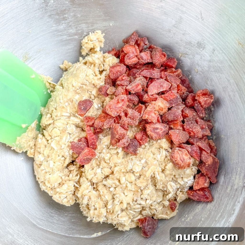 Strawberry Oat Delight Cookies 4 Close-up of a mixing bowl filled with cookie dough, showing chunks of dried strawberries folded in.