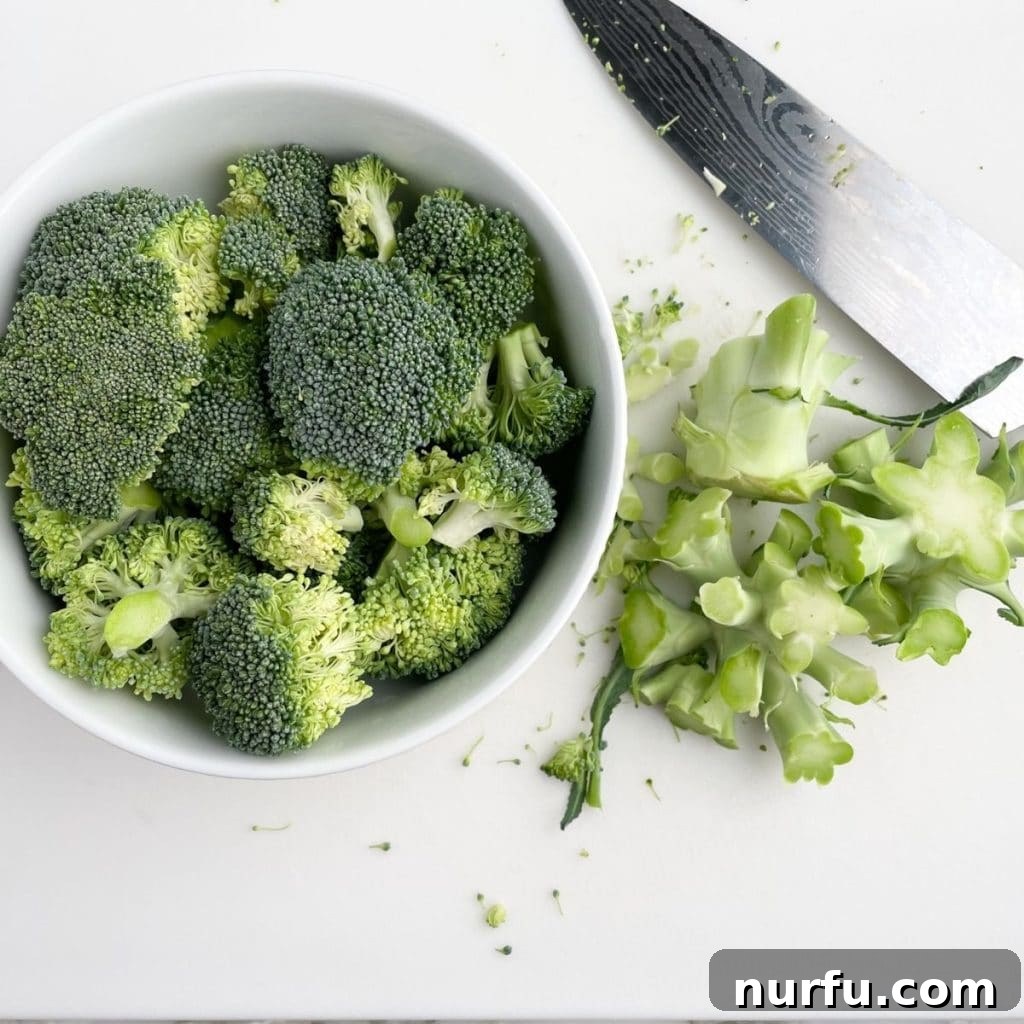 Achieve Perfectly Boiled Broccoli 3 Fresh broccoli florets neatly arranged in a bowl, with the remaining broccoli stems and a knife resting on a cutting board, illustrating the preparation stage.