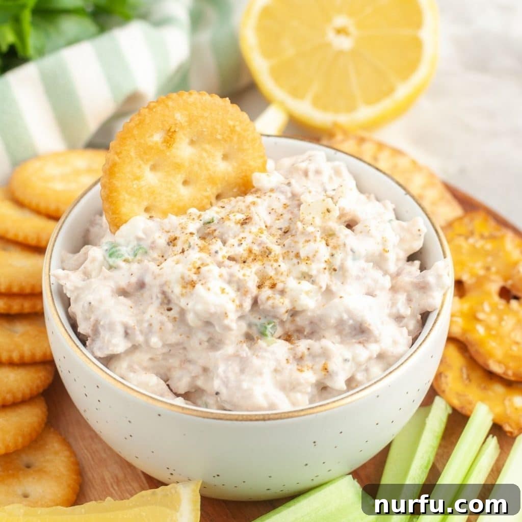 Lightning-Fast Savory Tuna Dip 2 A bowl of creamy tuna dip with a Ritz cracker delightfully dipped into it, ready to be enjoyed.