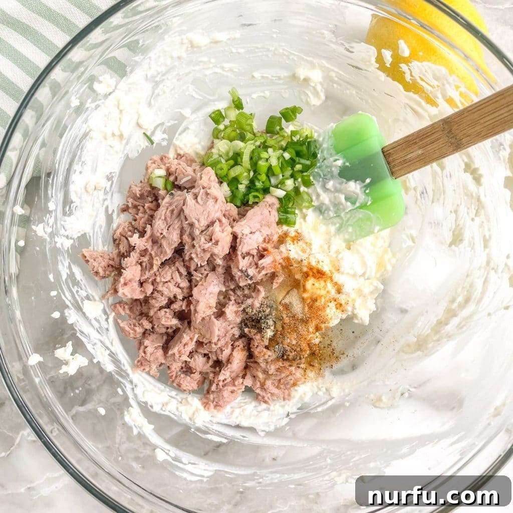 Lightning-Fast Savory Tuna Dip 3 A large mixing bowl containing flaked canned tuna, a generous dollop of mayonnaise, and freshly chopped green onions, poised for blending with a green spatula.