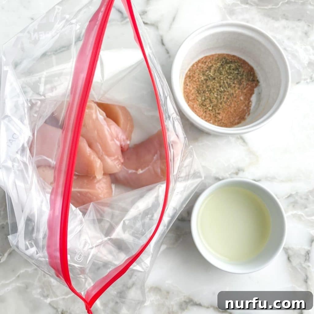 Raw chicken tenders marinating in a zip-top bag with olive oil and spices.