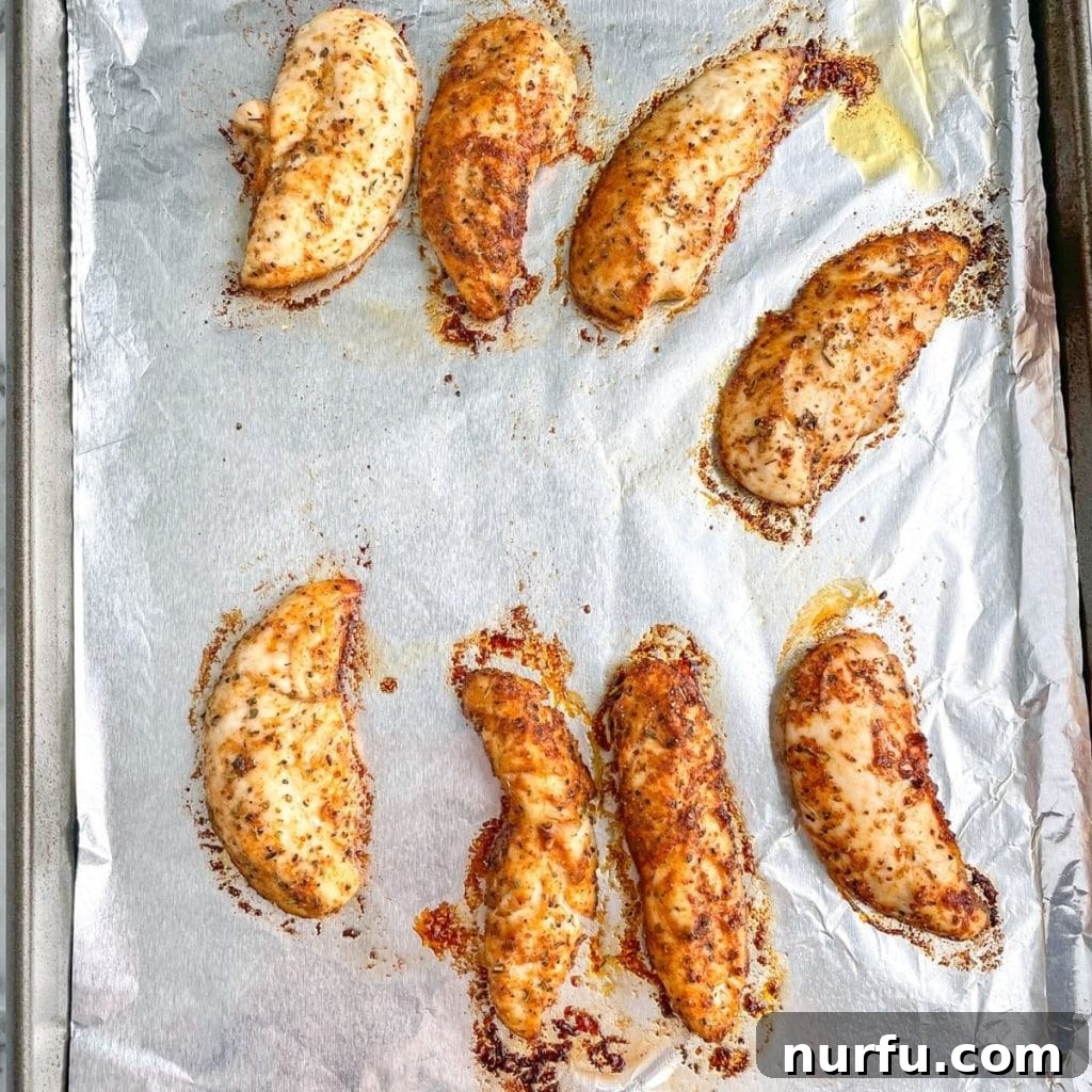 Cooked, golden-brown chicken tenders on a foil-lined baking sheet, fresh out of the oven.