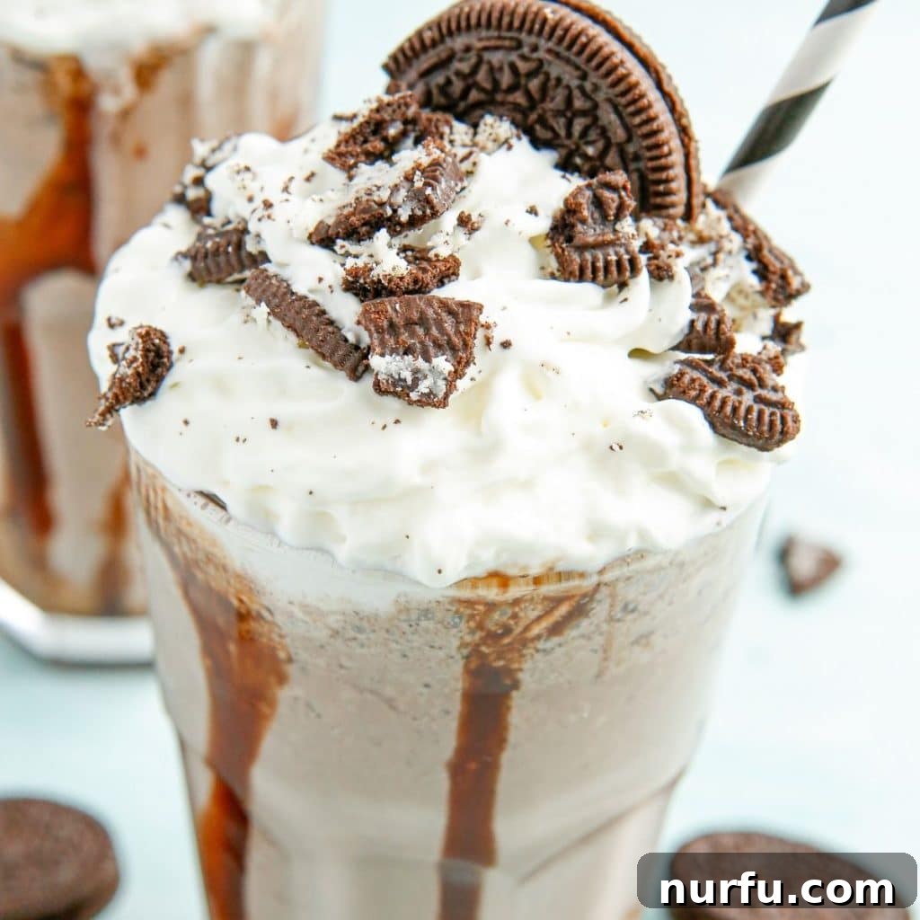 A refreshing glass of OREO milkshake with a straw, garnished with crushed OREOs and whipped cream.