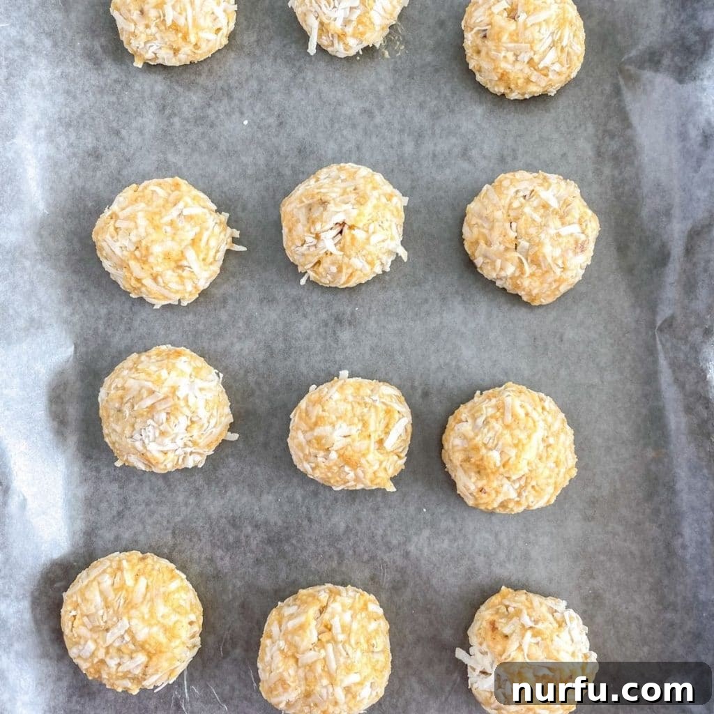 Zesty Orange Coconut Delights 5 Freshly rolled orange coconut balls, evenly coated in sweet coconut flakes, neatly arranged on a baking sheet lined with wax paper, ready for chilling.