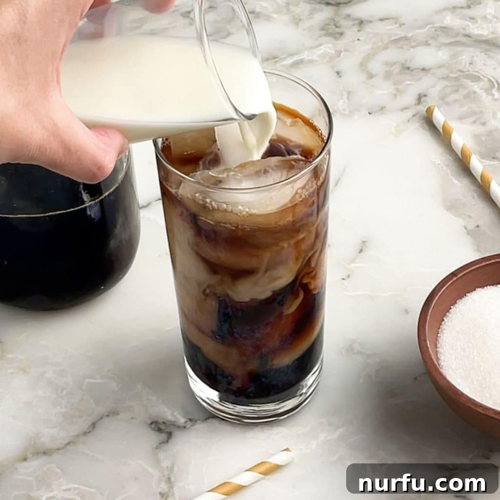 Crafting Perfect Iced Coffee at Home 4 Cream pouring into a glass of iced coffee, creating a beautiful marbling effect before stirring.