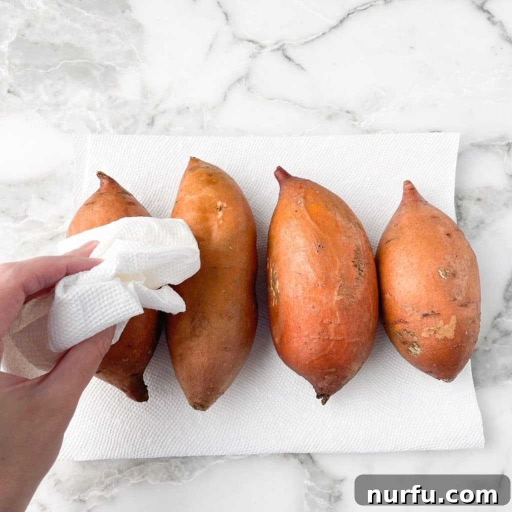 Mastering 400 Degree Sweet Potatoes Bake Time Revealed 4 A hand gently patting a clean sweet potato dry with a paper towel on a cutting board.