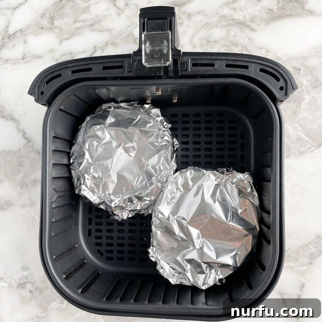 Two foil-covered mini pot pies neatly placed in an air fryer basket.