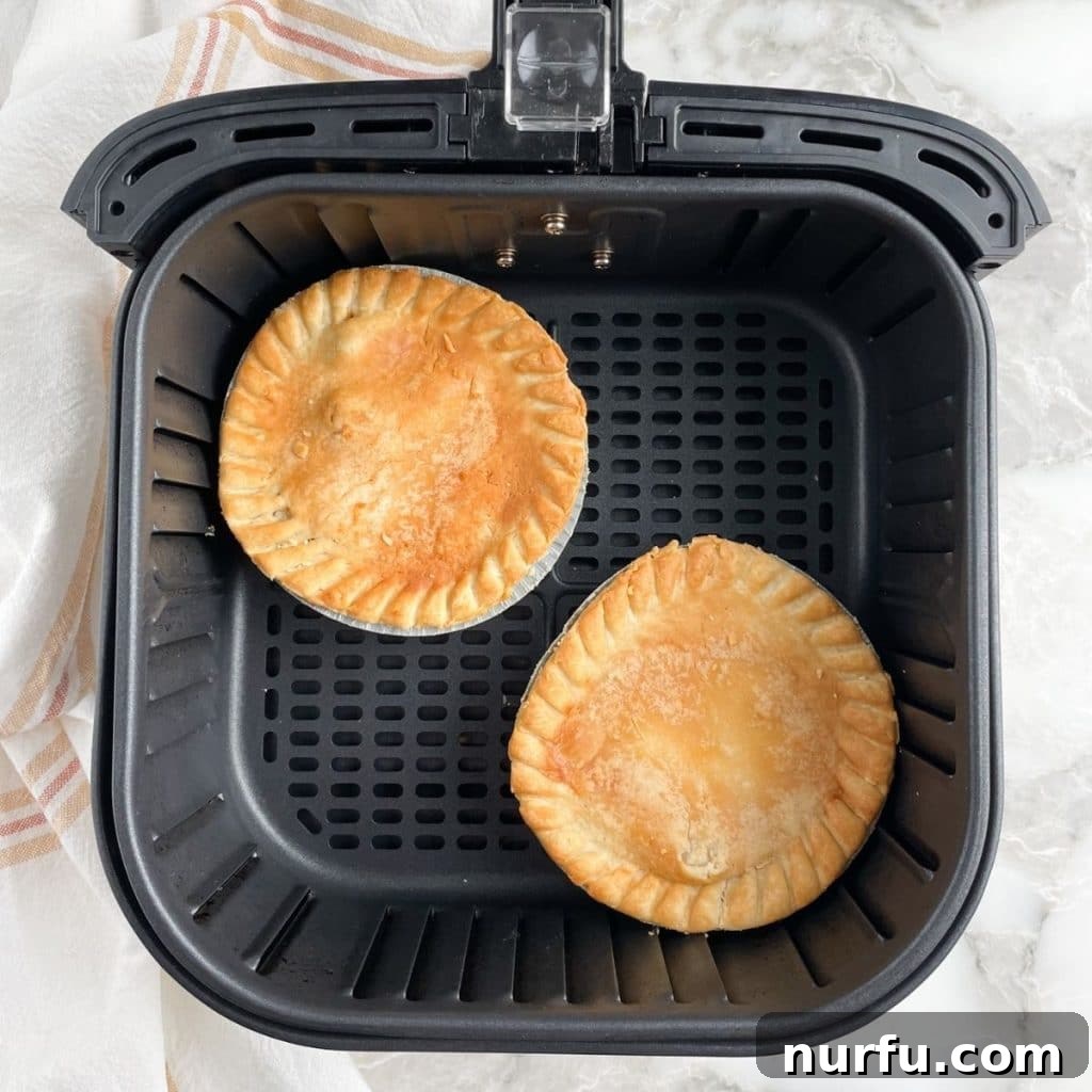 Two mini pot pies, with golden-brown crusts, cooking in an air fryer basket.