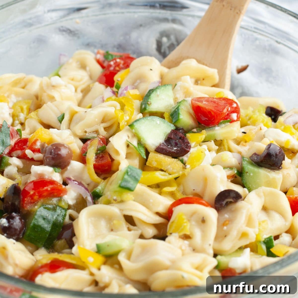 50 Refreshing Cold Lunch Ideas 11 A bowl of vibrant tortellini pasta salad with a wooden spoon, showcasing fresh vegetables and cheese tortellini.