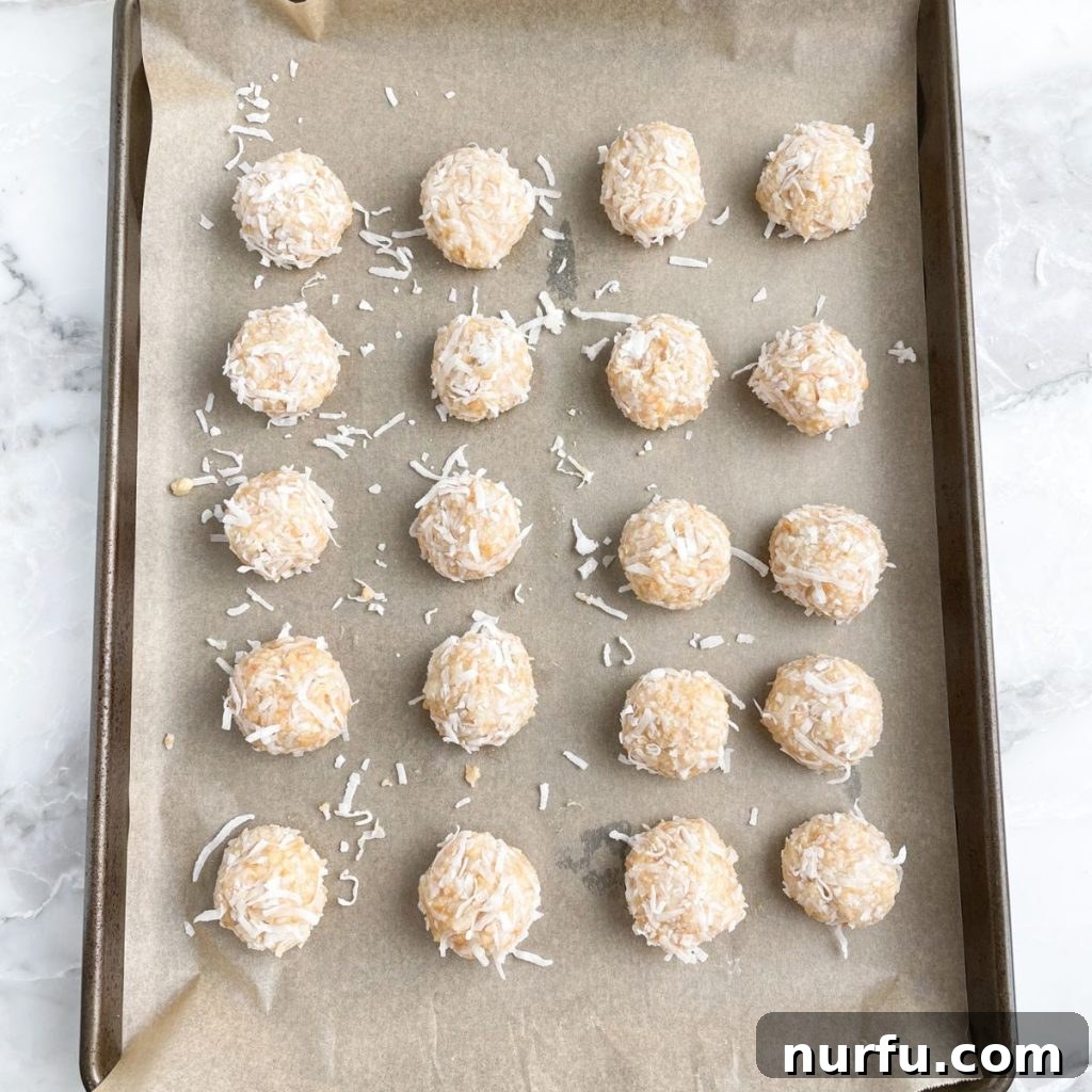 Zesty Coconut Lime Bites 5 Numerous perfectly formed lime coconut balls, freshly coated with shredded coconut, neatly arranged on a baking sheet, ready for chilling.