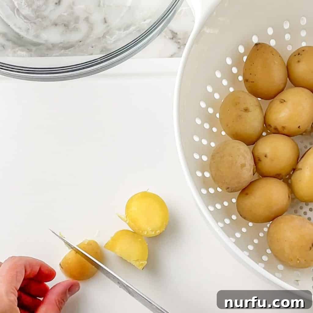 Boiling Potatoes for Perfect Potato Salad 4 A hand is shown cutting boiled potatoes into consistent chunks on a cutting board, ready for the next step of the potato salad preparation.