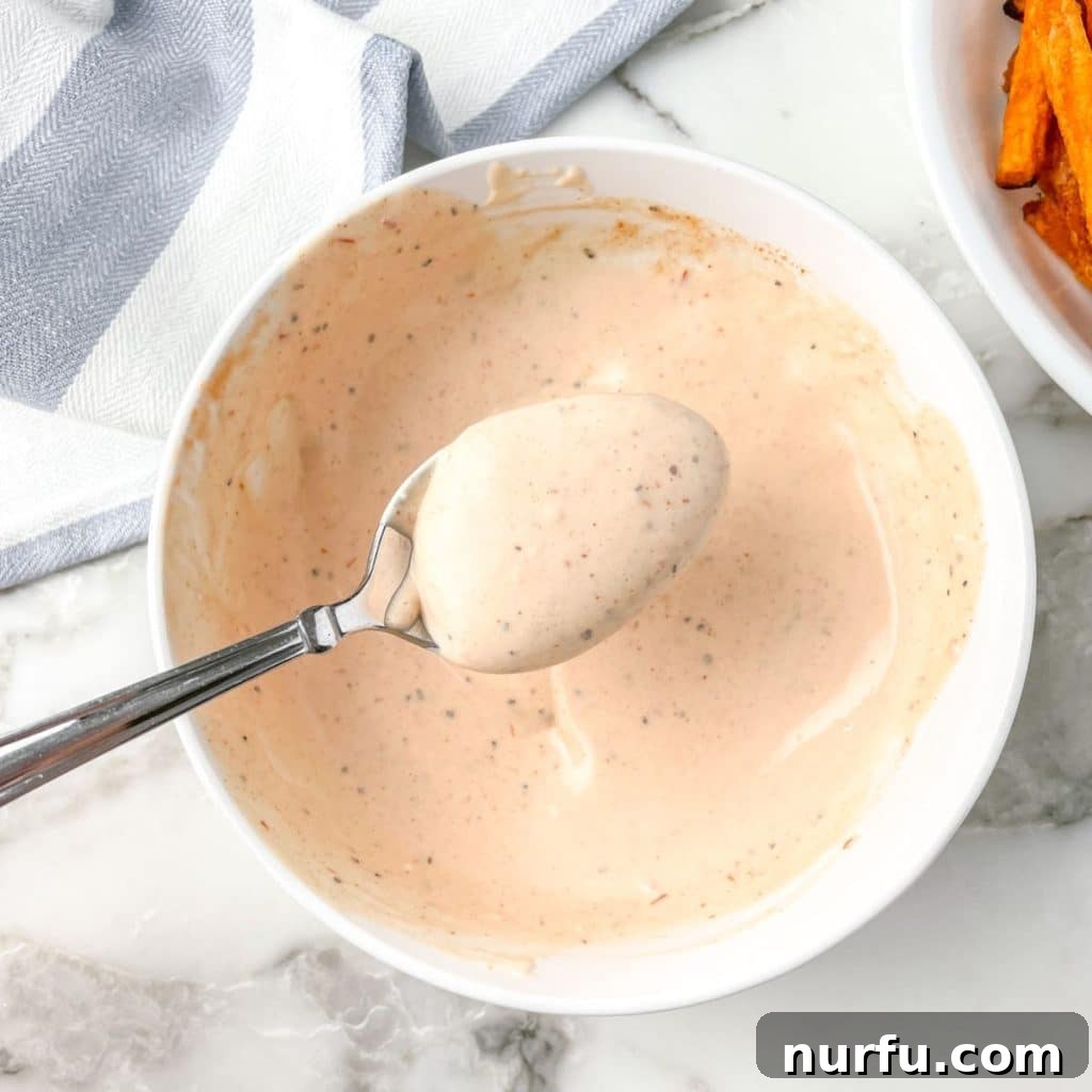 Sweet Potato Fry Dipping Bliss 4 A spoon stirring a bowl of creamy, orange-hued mayonnaise sauce, demonstrating the final mixing step for the sweet potato fries dipping sauce.