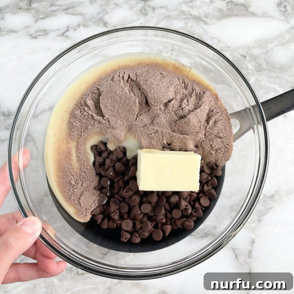 A bowl on a double boiler, filled with melting butter, chocolate chips, and hot cocoa powder, stirring to combine.