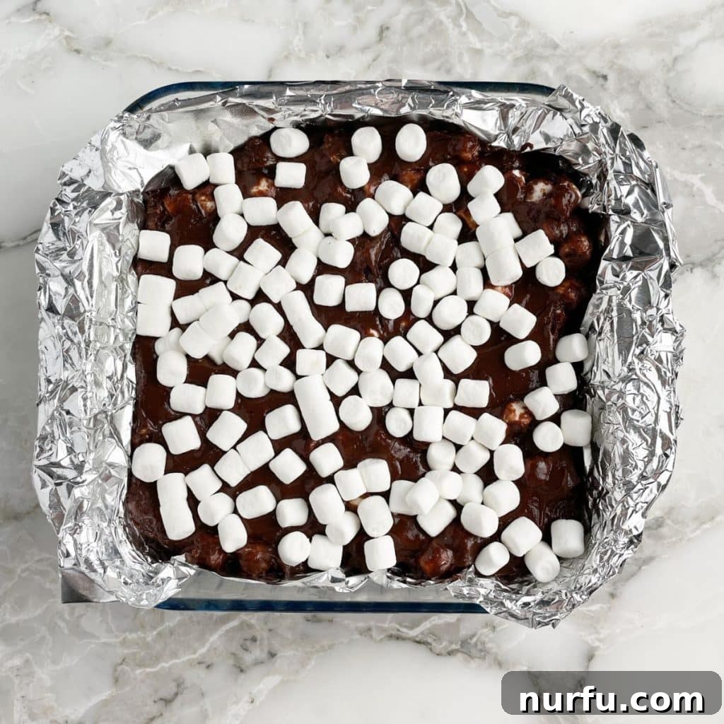 A pan filled with freshly made hot chocolate fudge, generously topped with mini marshmallows, chilling to set.