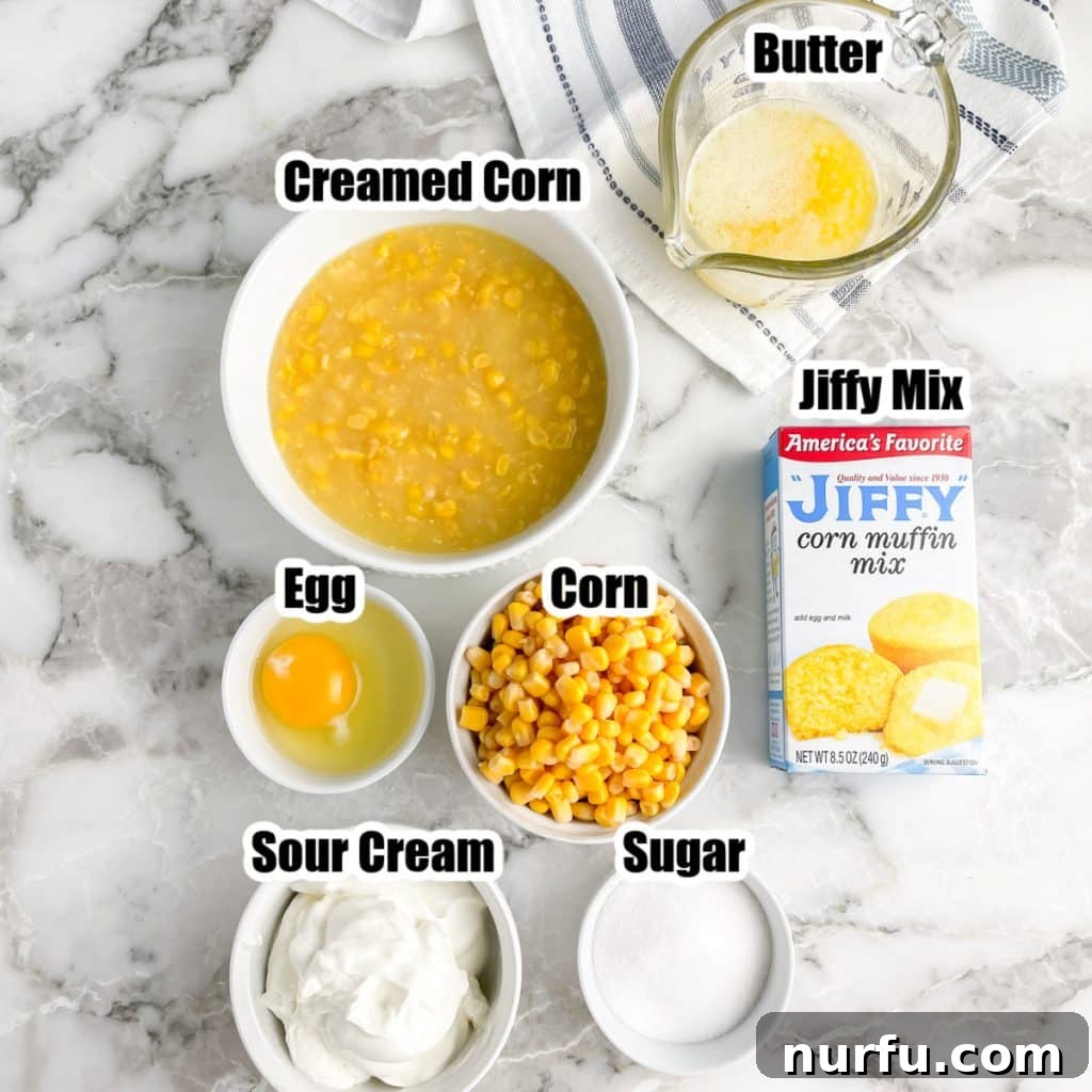 Jiffy Sweet Corn Bake 3 Individual ingredients for Jiffy corn pudding laid out: a bowl of corn, melted butter, an egg, sour cream, sugar, and a box of Jiffy corn mix.