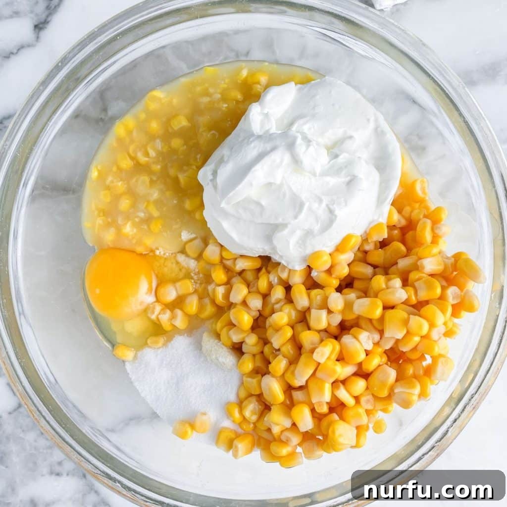 Jiffy Sweet Corn Bake 4 A large mixing bowl containing sour cream, whole kernel corn, creamed corn, an egg, and sugar, ready to be combined.