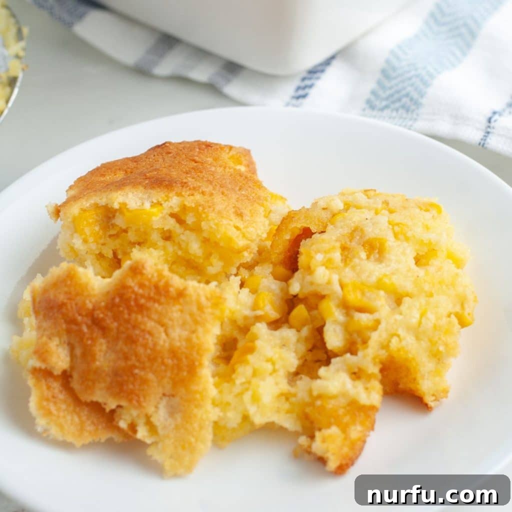 Jiffy Sweet Corn Bake 6 A serving of golden, creamy Jiffy corn casserole on a white plate, ready to be enjoyed as a side dish.