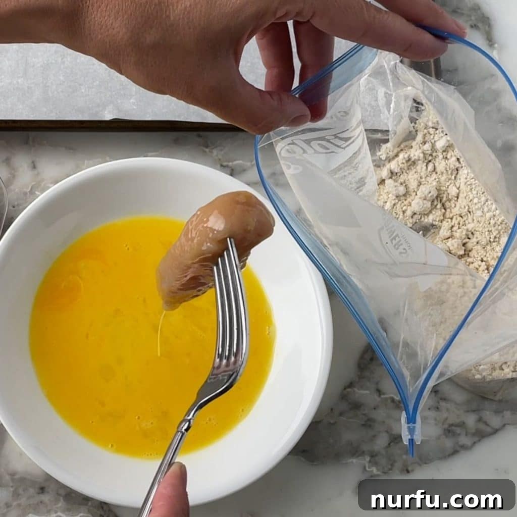 Crispy Bisquick Chicken Tenders 4 Raw chicken tenderloin being dipped into whisked eggs, a crucial step before breading.