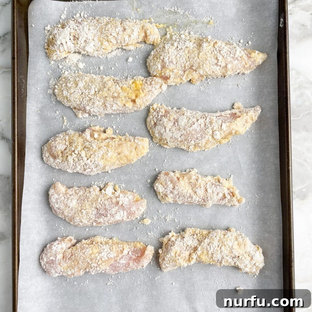 Crispy Bisquick Chicken Tenders 5 Sheet pan filled with evenly spaced, breaded chicken tenders, ready for baking.