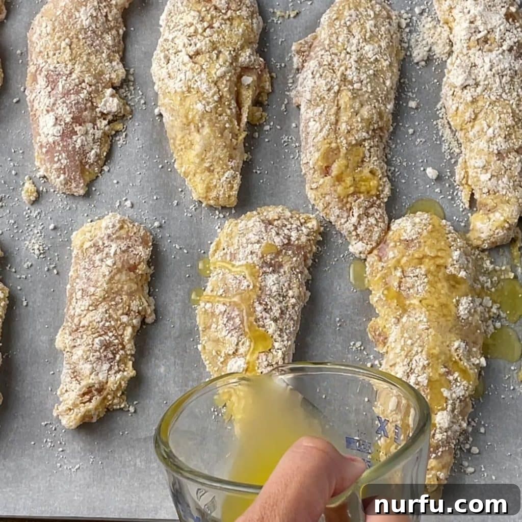 Crispy Bisquick Chicken Tenders 6 Melted butter being drizzled generously over breaded chicken tenders on a baking sheet before baking.