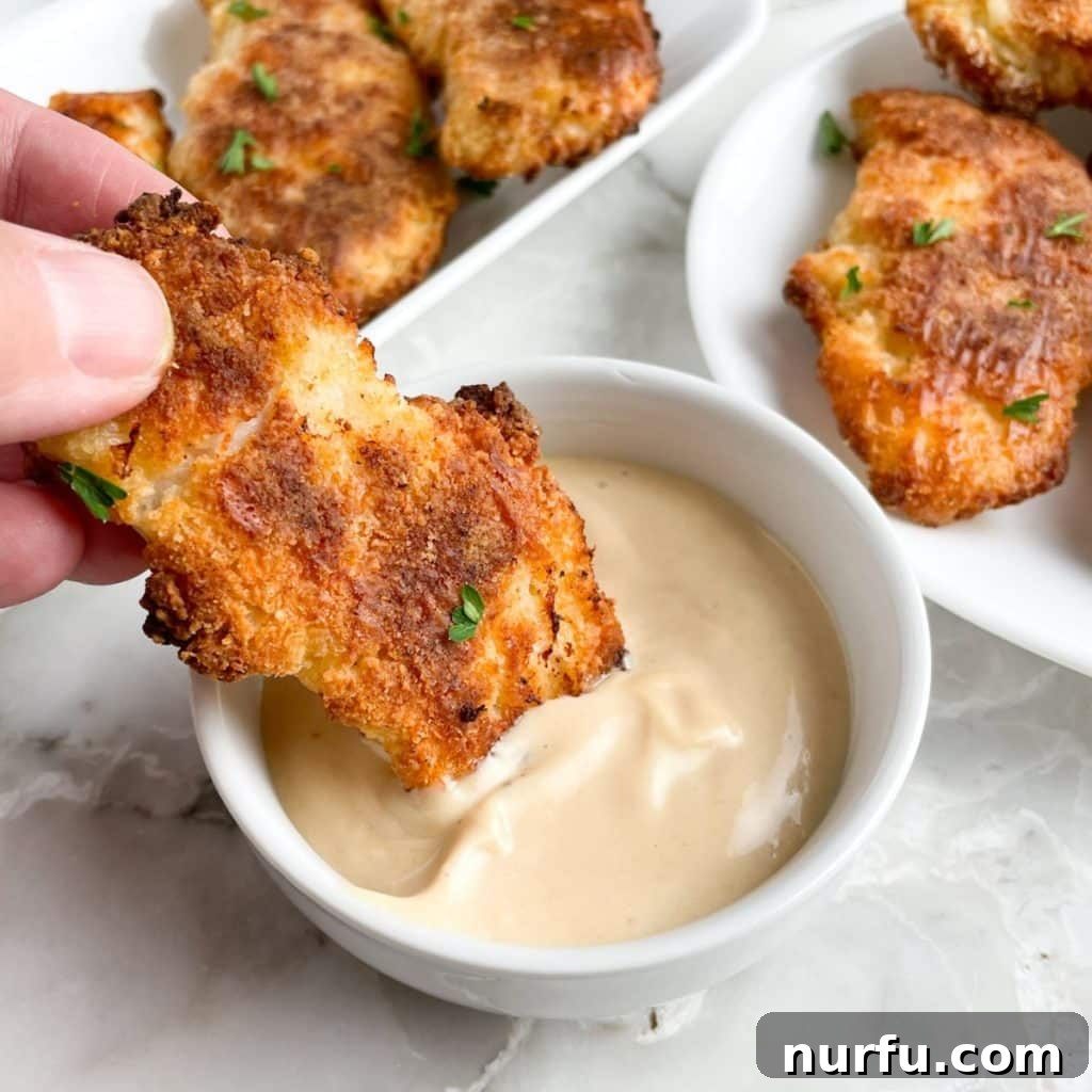 Crispy Bisquick Chicken Tenders 7 Crispy breaded chicken tenders being dipped into a vibrant red dipping sauce.
