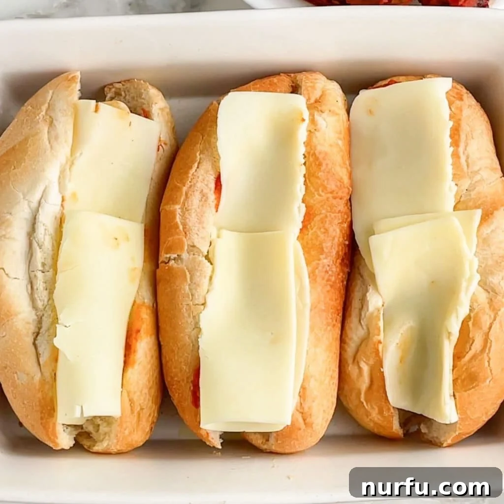 Sandwich rolls in casserole dish topped with mozzarella cheese, ready to melt.