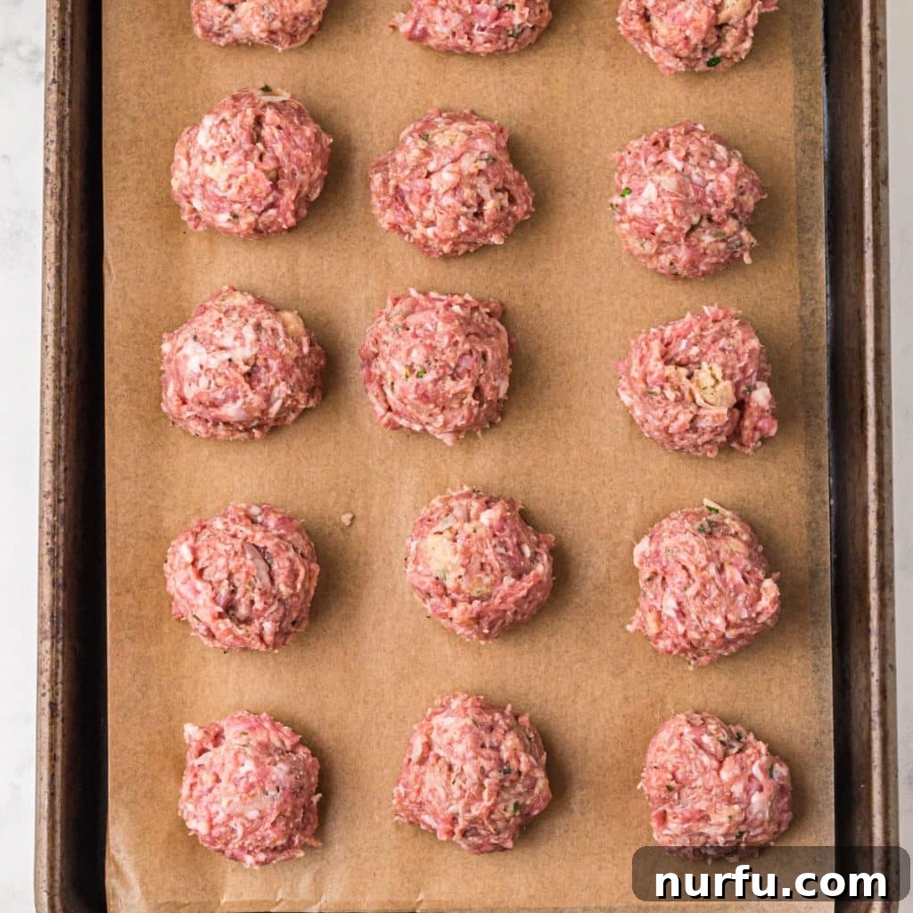 Irresistible Swedish Meatballs 5 Uncooked Swedish meatballs perfectly formed and neatly arranged on a parchment-lined baking sheet, ready for the oven.
