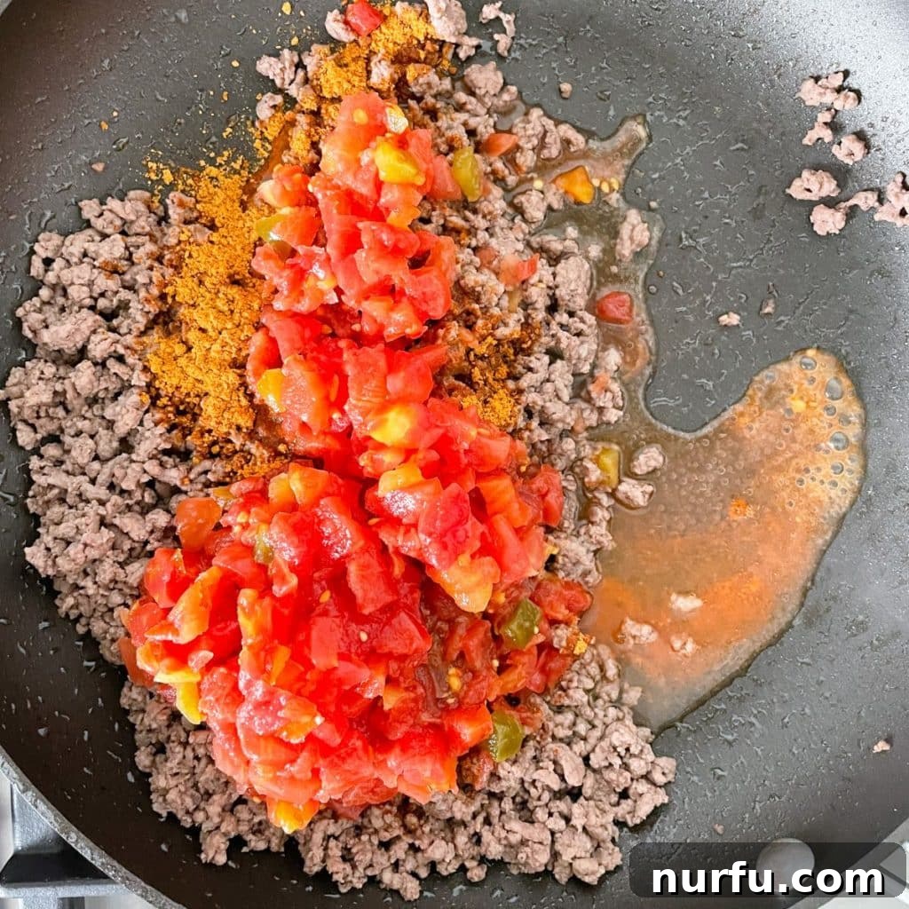 Loaded Ground Beef Taco Fiesta Dip 5 A close-up of a skillet filled with perfectly browned ground beef mixed with diced tomatoes and spices, ready for the next step of the taco dip recipe.