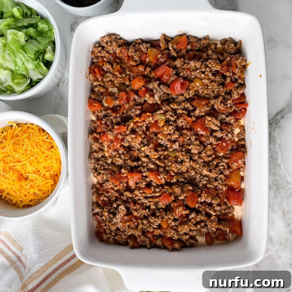 Loaded Ground Beef Taco Fiesta Dip 6 A casserole dish generously filled with layers of creamy taco dip and seasoned ground beef, ready for the final toppings and serving.