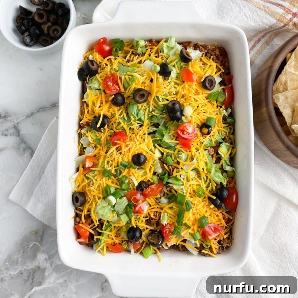 Loaded Ground Beef Taco Fiesta Dip 7 A casserole dish filled with the finished ground beef taco dip, showcasing all its delicious layers and colorful toppings.