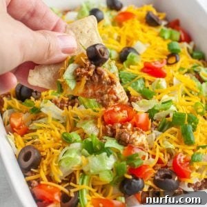 Hand holding tortilla chip with beef taco dip.