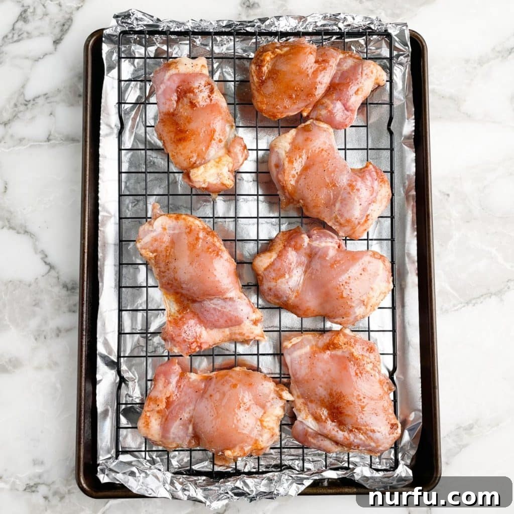 Sticky BBQ Chicken Thighs 6 Uncooked, seasoned chicken thighs neatly arranged on a wire rack over a baking sheet, ready for the oven.